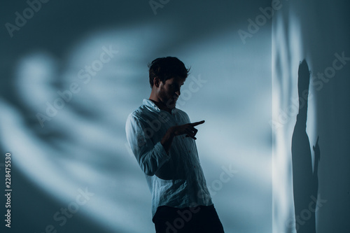 Man with schizophrenia standing alone in a room pointing at his shadow on the wall, real photo with copy space photo
