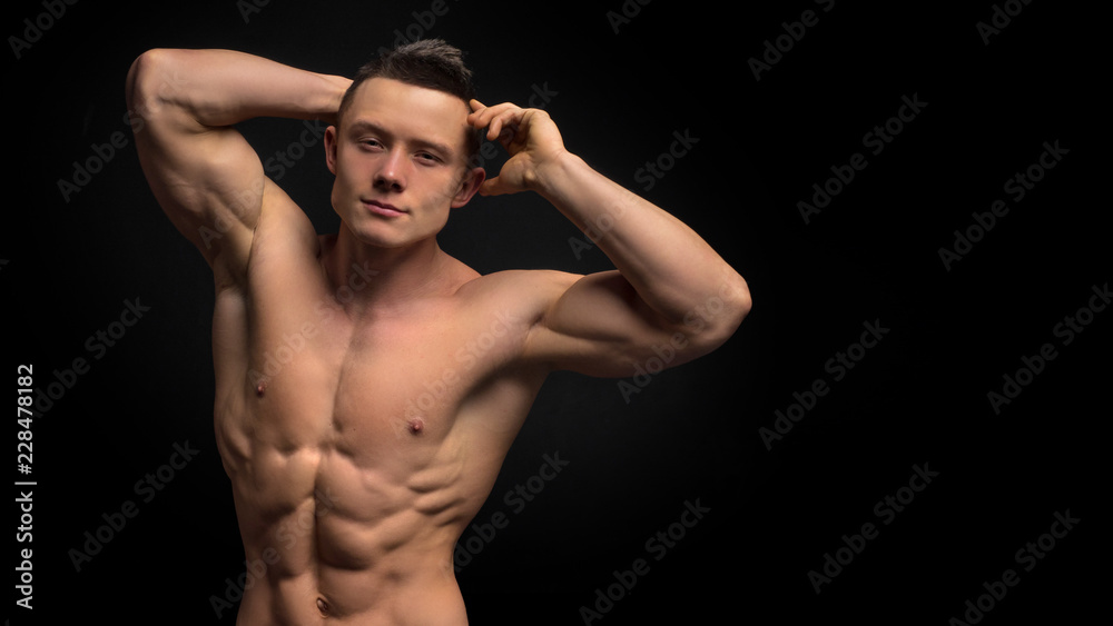 Handsome slim man with muscular body. Closeup of fit young man's abdomen against dark background.
