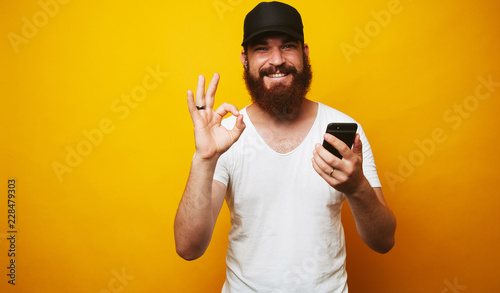 Man with beard holding phone and showing OK gesture photo