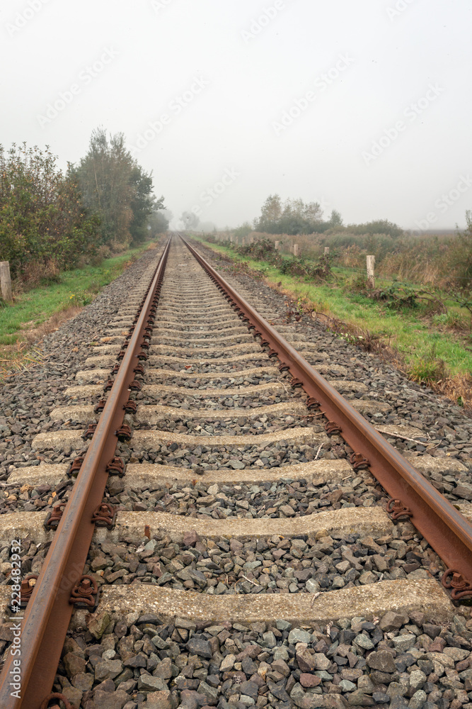 Rusty seemingly endless single track train tracks through a rural Dutch area with early morning fog Rusty seemingly endless single track train tracks through a rural Dutch area with early morning fog