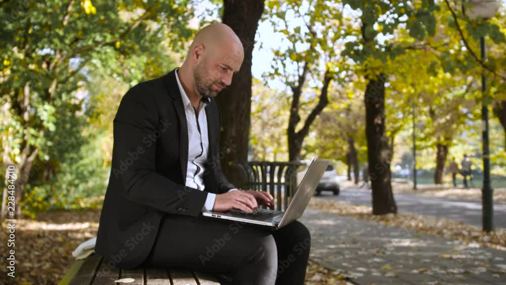 Handsome businessman typing on the laptop in the park Handsome businessman typing on the laptop in the park