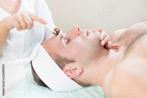 The man undergoes the procedure of medical micro needle therapy with a modern medical instrument derma roller. 