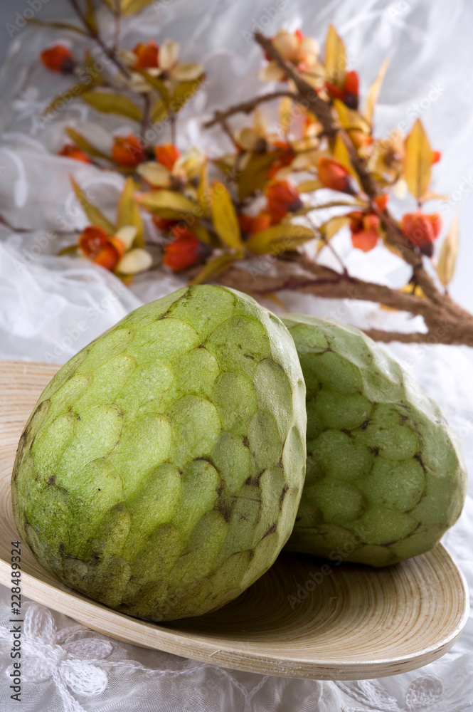 Fototapeta premium Two custard apples on a wooden plate, with a branch in the background.