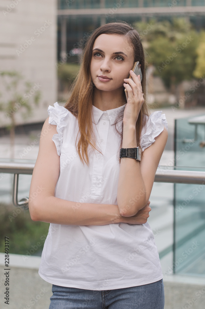 Young european female with brown hair, in white blouse and blue jeans calling via mobile phone with very concentrated and attentive face expression. Communication and mobile phone calls