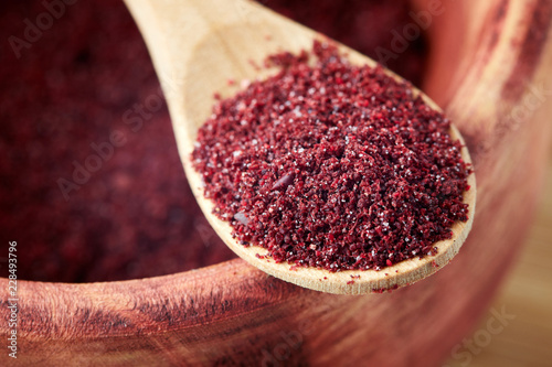 Close up of ground sumac spice powder in wooden spoon photo