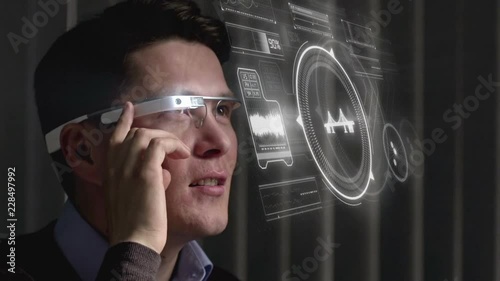 Close up of cheerful Asian man using the touch pad built on the side of smart glasses and looking at virtual interface projected in the air photo