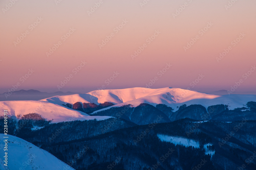 Amazing sunrise in the mountains in winter. Snow-covered peaks of mountains in the rays of the sunrise in the winter frosty morning.
