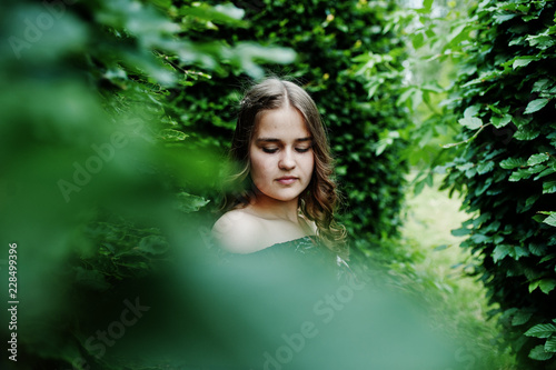 Portrait of a fabulous young girl in pretty dress with stylish curly hairstyle posing in the forest or park.