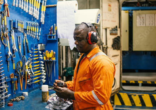 African marine engineer officer in engine control room ECR. He works in workshop with equipment photo