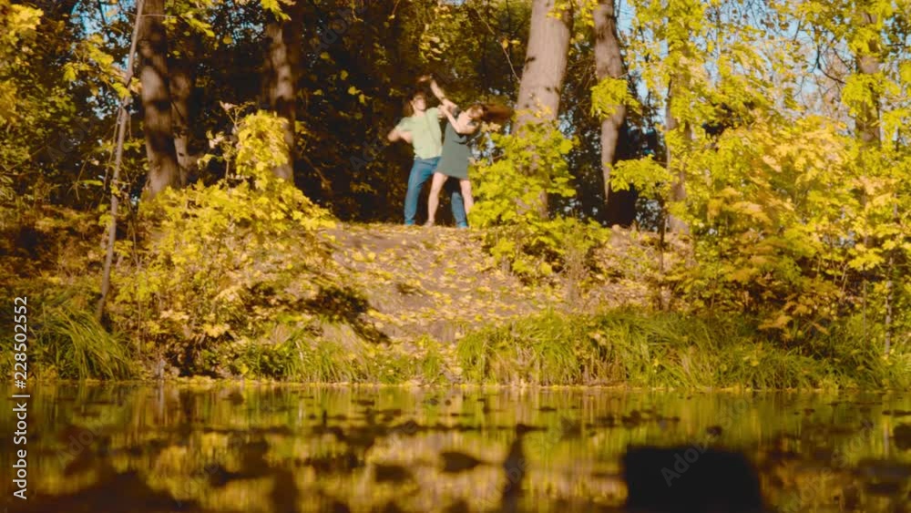 Young happy couple dancing on the bank of the lake. Sunny day, golden autumn. Wide shot Young happy couple dancing on the bank of the lake. Sunny day, golden autumn. Wide shot