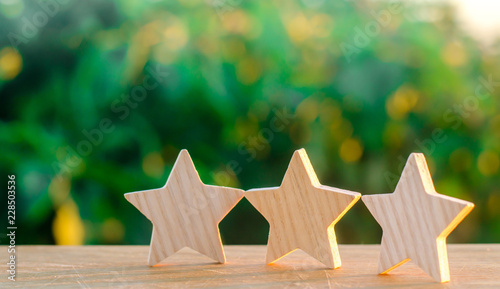 Three wooden stars on a green bokeh background. The concept of the rating of hotels and restaurants, the evaluation of critics and visitors. Quality level, good service. selective focus