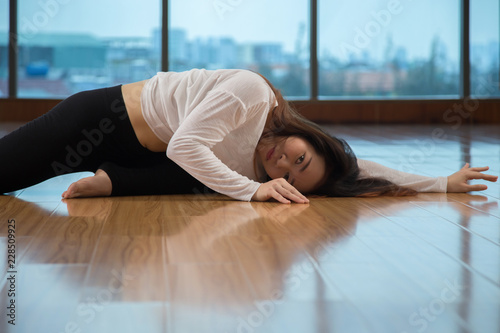 Side view of attractive Asian female lying on floor and looking at camera while dancing in stylish studio