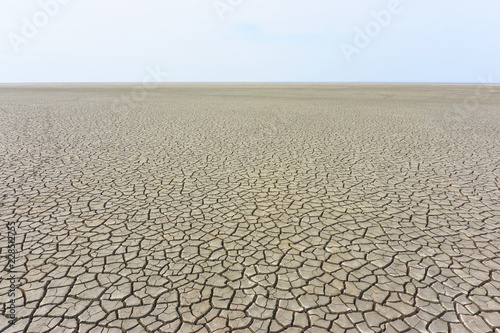 Desolate landscape with cracked ground at the seashore. Brown, beige, light tan and grey colored. Concept of global warming.