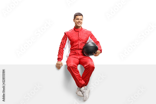Racer in a suit holding a helmet and sitting on a panel