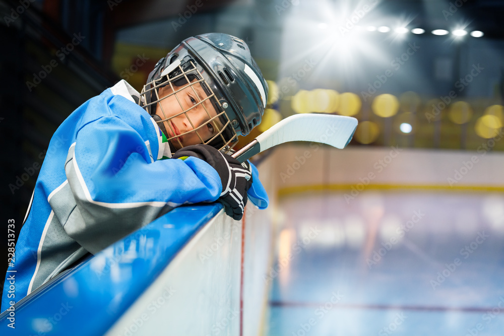 Naklejka premium Teenage hockey player leans on the boards of rink