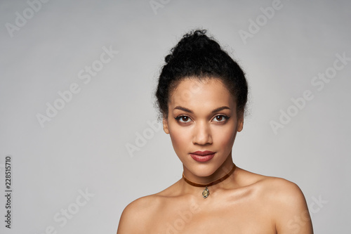 Beauty closeup portrait of beautiful mixed race woman wearing chocker looking at camera, isolated on gray background