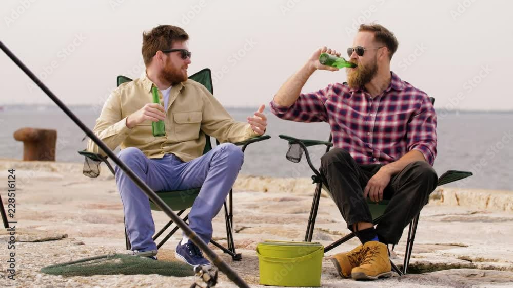 leisure and people concept - happy friends fishing and drinking beer on pier leisure and people concept - happy friends fishing and drinking beer on pier