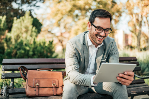 Smiling business man using tablet while sitting on the bench.