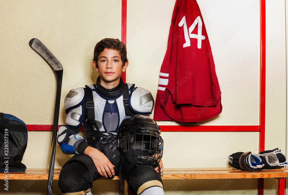 Fototapeta premium Boy sitting on the bench in ice hockey locker room