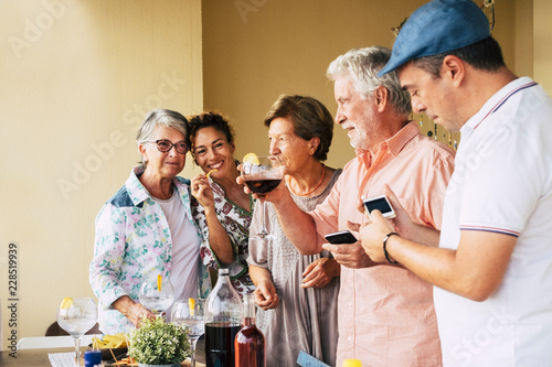 People group with mixed ages and sex having fun together in friendship for a dinner or lunch. Men playing with phone and technology. Smiles and cheerful concept