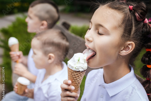 adorable lovely children eating ice cream sitting on a wooden bench in the park. fun holiday concept