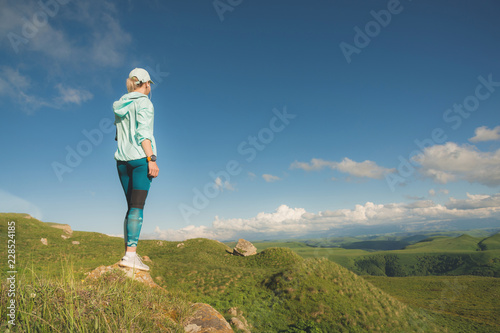 Attractive sports girl in a cap and headphones before jogging in a picturesque location. Workout outdoors. Back view