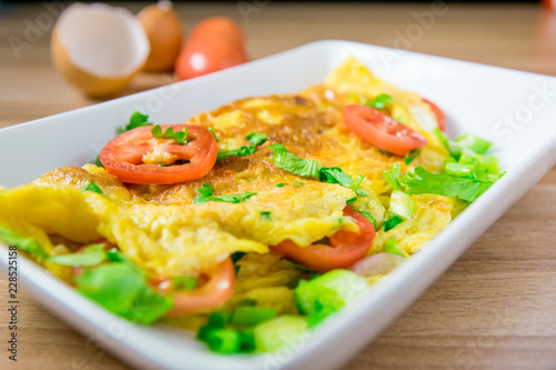 A photo of an omelette with cherry tomatoes, parsley. and grated cheese, shot from above on a rustic wooden texture with a place for text