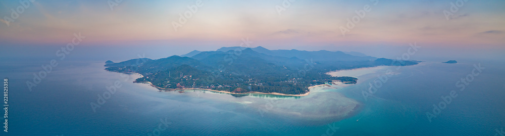 Panorama lone standing island. Sunset aerial drone shot. Ko Pha-ngan. Thailand. Overwhelmed view from above Ko Pha-ngan island and the ocean at the colorful sunset. The Kingdom of Thailand.