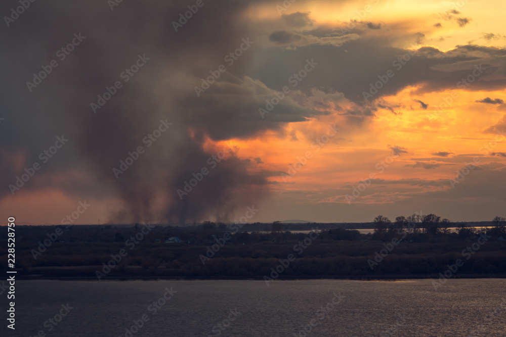 environmental problem of fire on dry grass with smoke onthe horizon inflated by a strong wind during the sunset