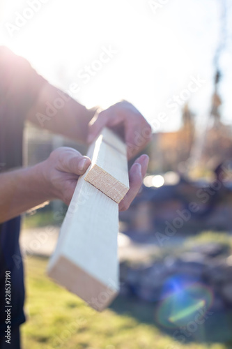 A man holds in his hands two wooden blanks and compares their size, on a warm summer day in the sun, outdoors.