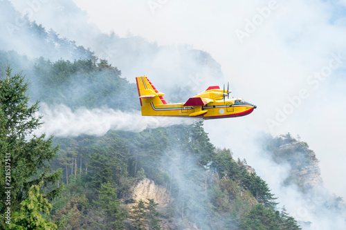 Water bomber aircraft Canadair. A yellow airplane of the Fire Brigade flying over a wildfire in a pine forest.