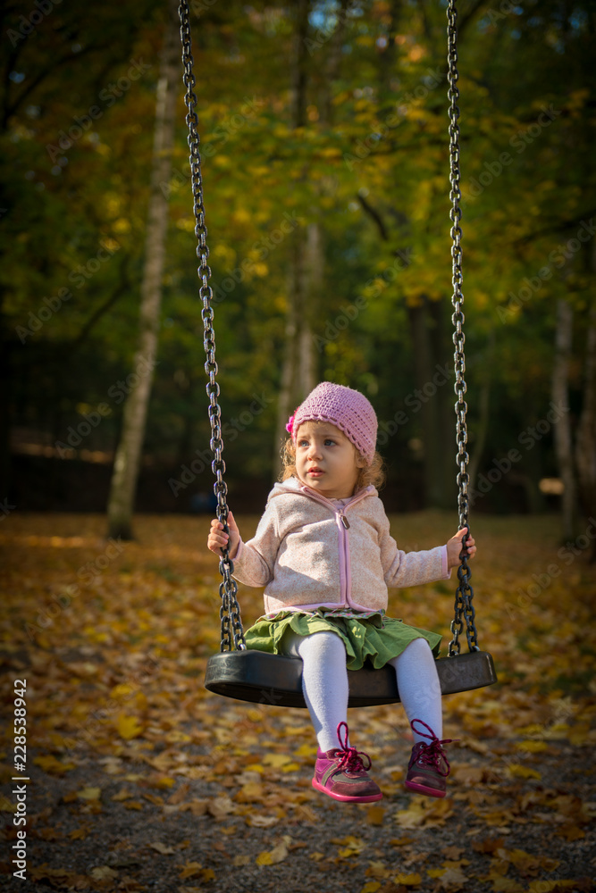 Little girl playing in Autumn park swing