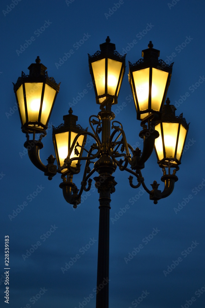 Iron lamppost with five yellow lights at night on blue sky