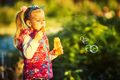 Pretty little girl and soap bubbles in autumn park