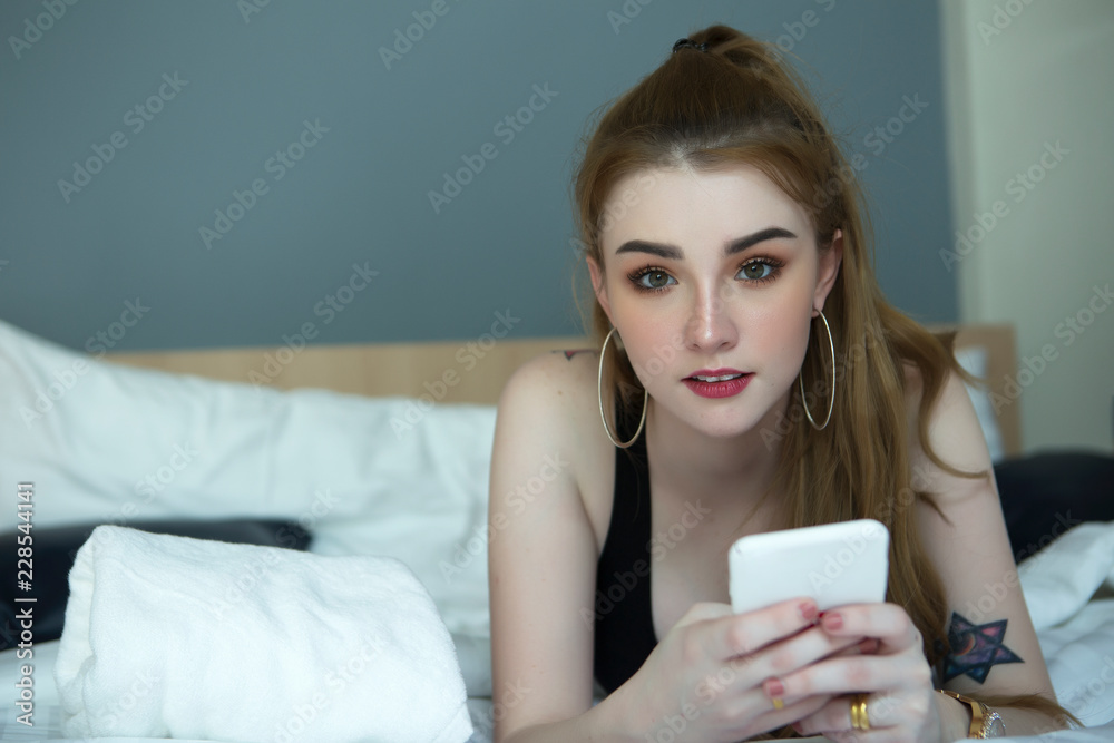 The beautiful girl is using her phone in the bedroom or in the hotel room. The beautiful girl is using her phone in the bedroom or in the hotel room.