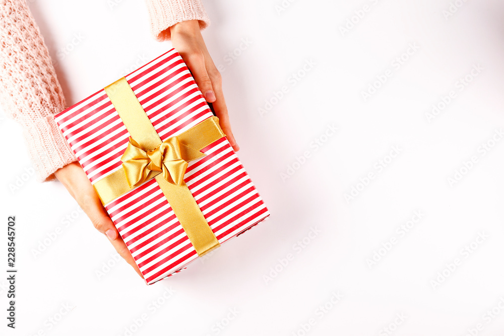 Fototapeta premium Top view of woman's hands wearing white knitted wool sweater, giving present wrapped in beautiful paper & tied with bow. Holiday greeting concept. Isolated background, copy space, close up, overhead.