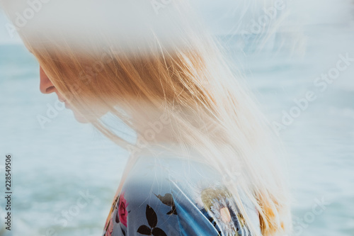 Close-up portrait of graceful blond woman in blue dress with sea in background
