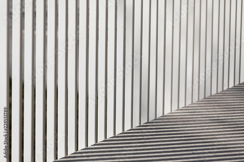 Shadows casted by a fence on a concrete sidewalk