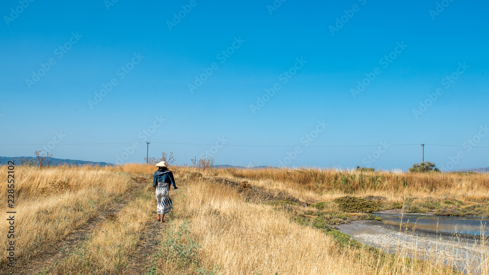 Woman walking down path through grasslands with large blue sky