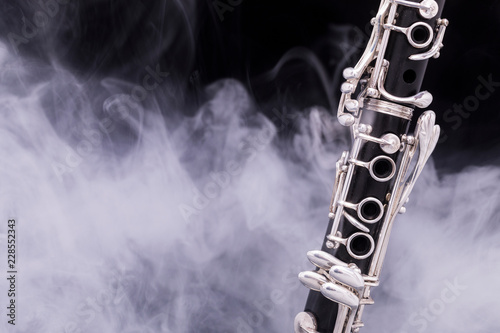 A black clarinet with silver plated keys in smoke on a black background