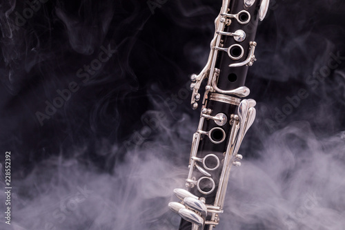 A black clarinet with silver plated keys in smoke on a black background photo