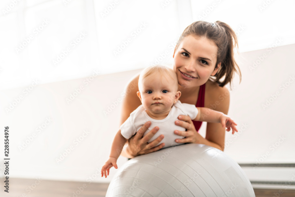 A Portrait of beautiful young mother in sports wear with her charming little baby in training session A Portrait of beautiful young mother in sports wear with her charming little baby in training session