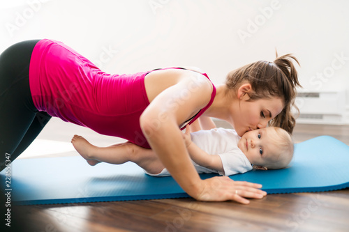 A Portrait of beautiful young mother in sports wear with her charming little baby in training session