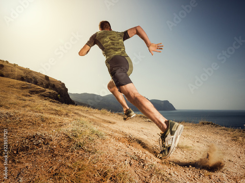 Young man runner running on a dusty country road. Jogger training workout in fitness shoe. Healthy lifestyle and sport concept.