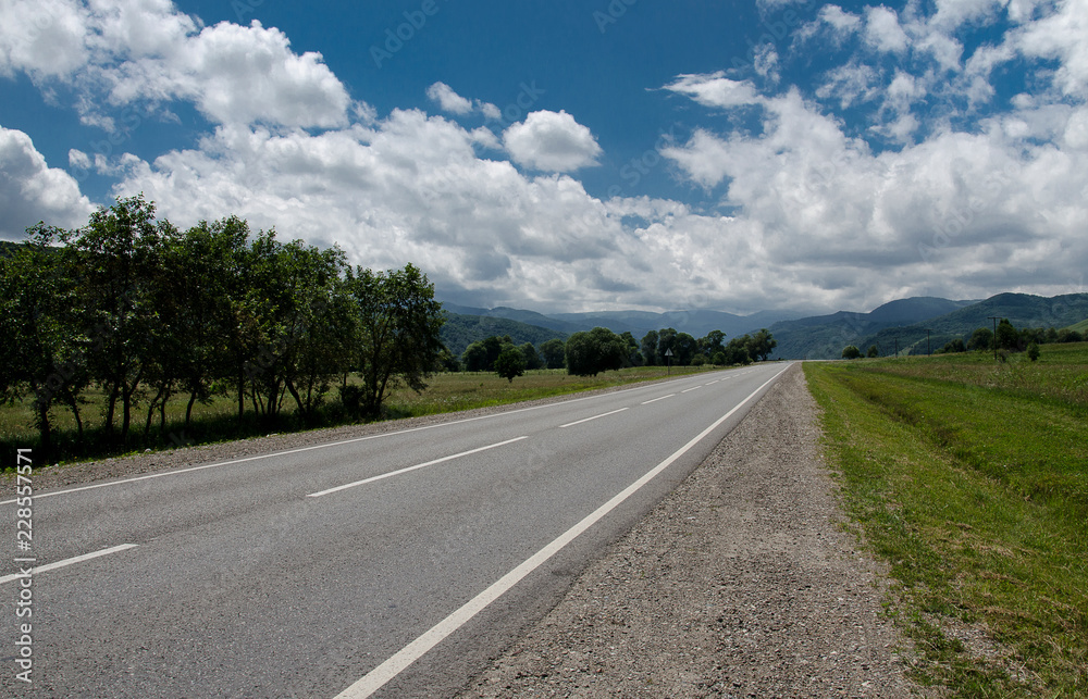 Empty asphalt road highway in the forested mountains, on the background a cloudy sky Empty asphalt road highway in the forested mountains, on the background a cloudy sky