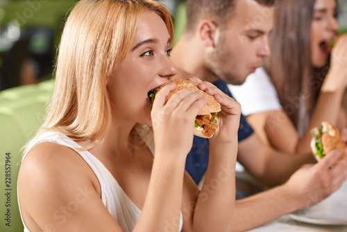 Side view of hungry blonde biting big juicy burger 