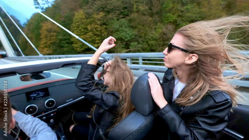Two beautiful young girls ride in a red cabriolet among the mountains ...