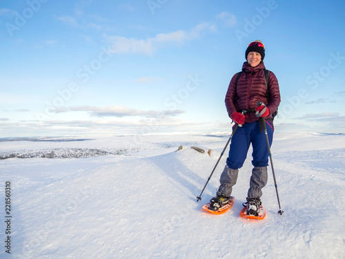 Pretty, young woman snowshoeing and enjoying splendid winter weather with abundance of snow