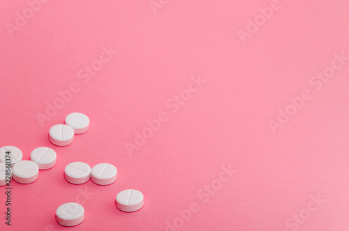 A lot of pills in the left-down corner of the pink background