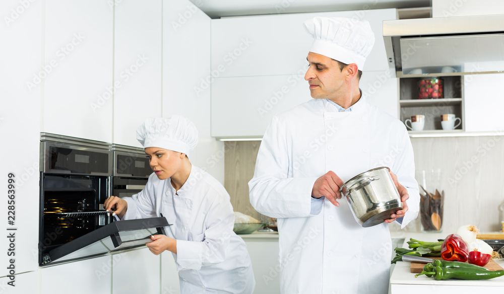 Professional chef  in uniform with pot  working with woman cook on kitchen
